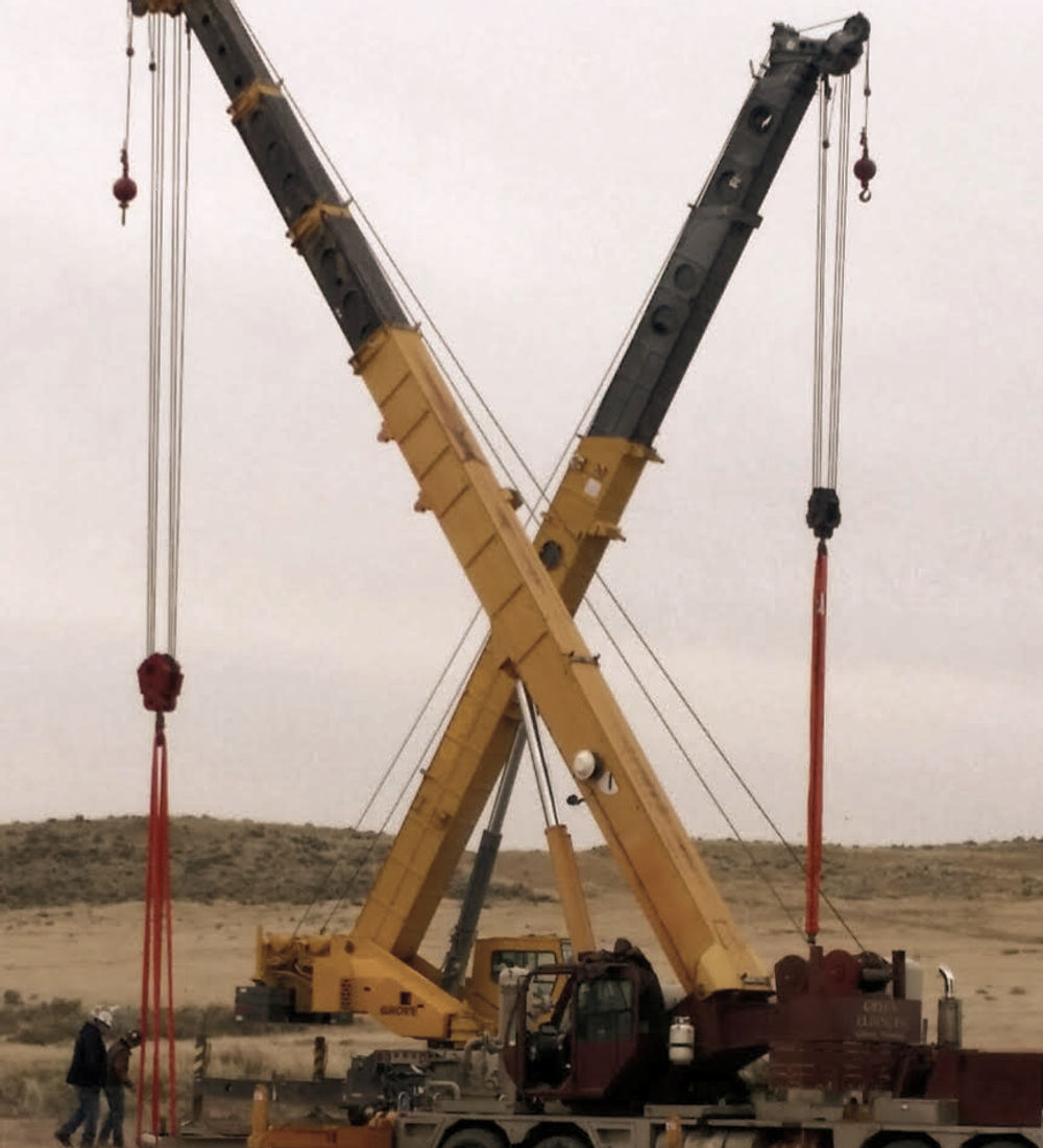 Two crane booms crossing against an overcast sky